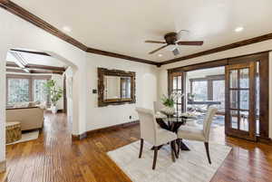 Dining room with hardwood / wood-style floors, ceiling fan, arched walkways, ornamental molding, and french doors
