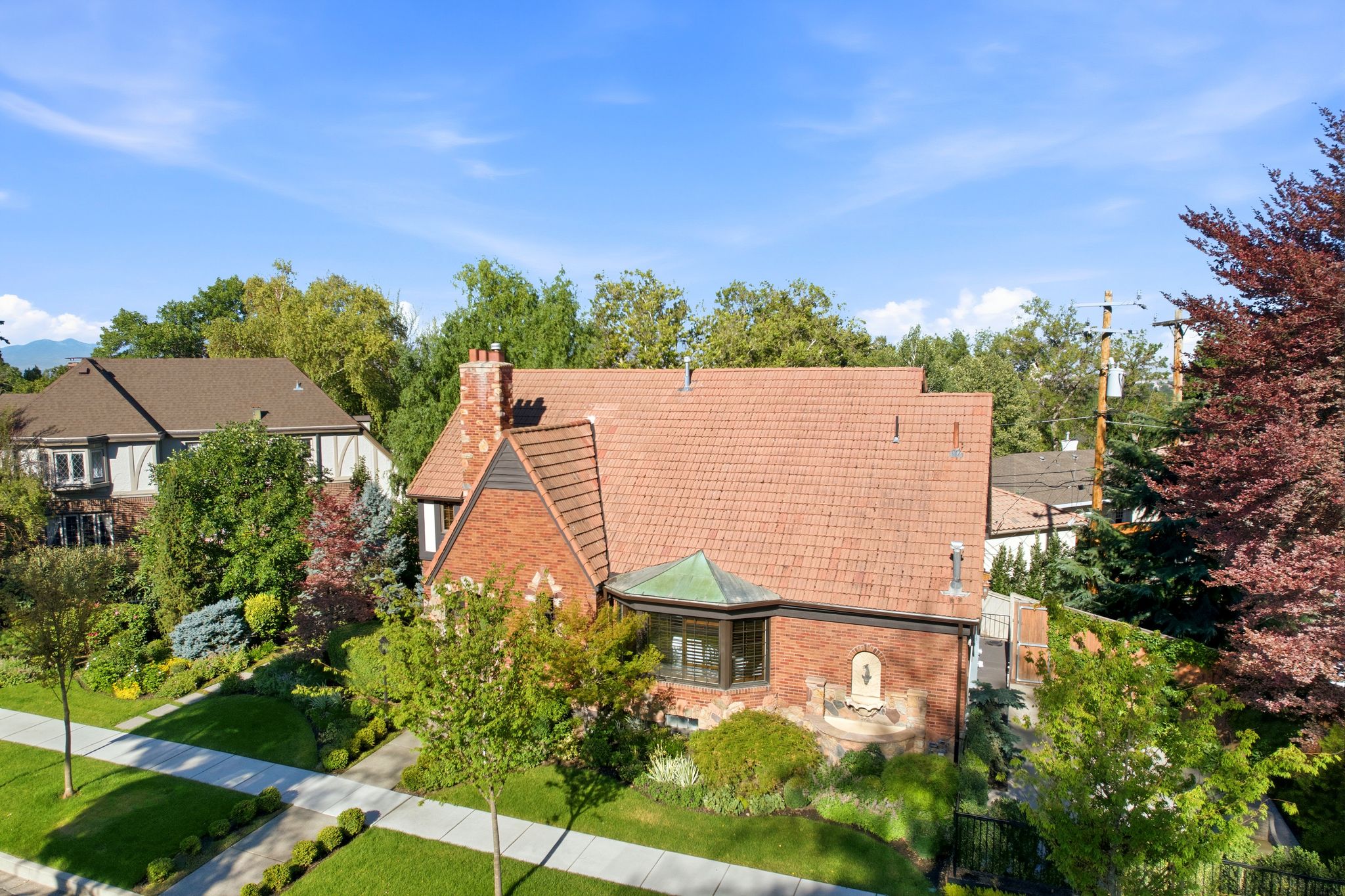 Brick residence featuring a terracotta-style tile roof, bay window with a copper-tone roof, brick chimney, and a stone wall fountain