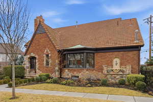 View of front of property featuring brick siding, a chimney, a front lawn, and a tile roof