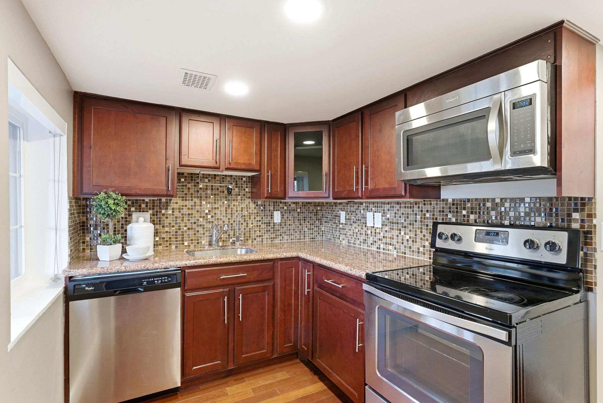 Kitchen with stainless steel appliances, light stone counters, light wood finished floors, glass fronted cabinets, and tasteful backsplash