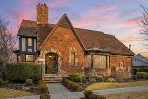View of front of property with a chimney, brick siding, stone siding, and a tiled roof