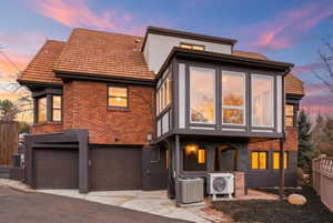 View of front of property featuring brick siding, a garage, a tile roof, asphalt driveway, and stucco siding