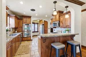 Kitchen with arched walkways, wood finish cabinetry, a kitchen breakfast bar, stainless steel appliances, and pendant lighting
