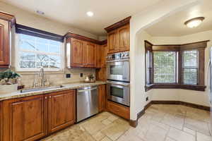 Kitchen featuring light stone counters, stainless steel appliances, stone tile flooring, wood finish cabinets, and recessed lighting