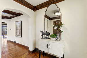 Hall featuring arched walkways, beamed ceiling, dark wood-type flooring, and ornamental molding