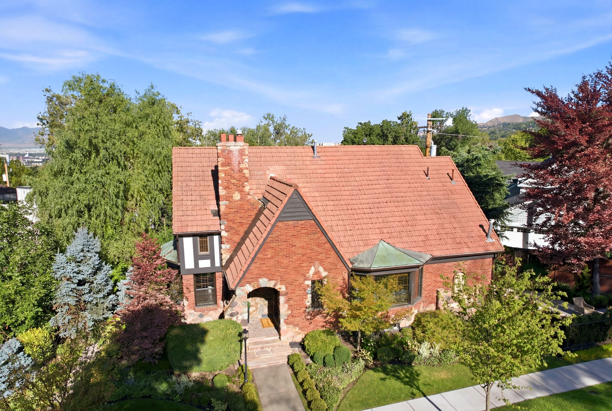 Brick and stone Tudor-style residence featuring a terracotta-colored tile roof, a prominent chimney, and a copper-patina bay window