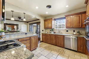 Kitchen with wood finish cabinets, stone tile flooring, stainless steel appliances, tasteful backsplash, and light stone counters