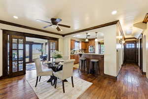 Dining room featuring dark wood-type flooring, arched walkways, a ceiling fan, and crown molding