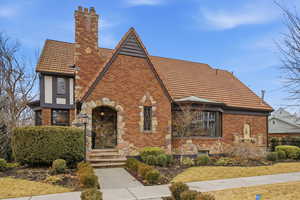 Tudor home with a chimney, brick siding, a tile roof, and stone siding