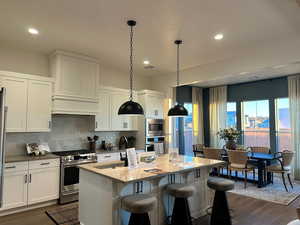 Kitchen with stainless steel appliances, white cabinets, hanging light fixtures, dark wood-style floors, and a kitchen island with sink