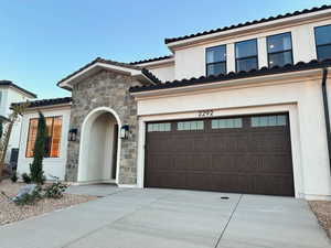 Mediterranean / spanish-style home with stone siding, stucco siding, and concrete driveway