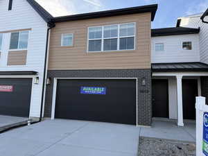 Contemporary home featuring brick siding, a garage, driveway, and a standing seam roof