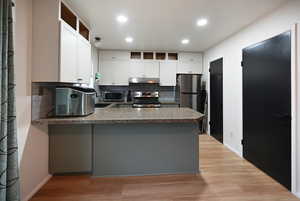 Kitchen featuring backsplash, a peninsula, stainless steel appliances, light wood-type flooring, and white cabinets