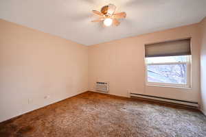 Carpeted empty room with baseboard heating, ceiling fan, and a textured ceiling
