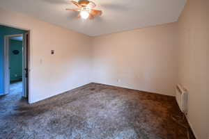 Spare room featuring dark carpet, a ceiling fan, and radiator