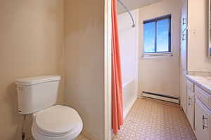 Bathroom with light floors, a baseboard heating unit, shower / bathtub combination with curtain, and vanity