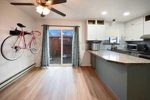 Kitchen with white cabinetry, light wood finished floors, baseboard heating, tasteful backsplash, and a peninsula