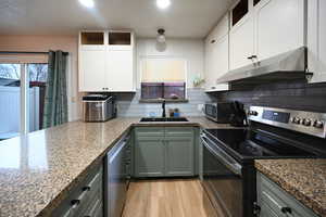 Kitchen featuring stainless steel appliances, light wood-type flooring, two tone cabinets, backsplash, and light stone countertops