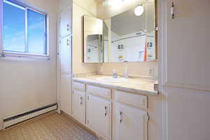 Bathroom featuring vanity, baseboard heating, light floors, and a shower
