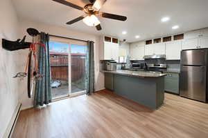 Two tone kitchen with stainless steel appliances, baseboard heating, a peninsula, tasteful backsplash, and two tone cabinetry