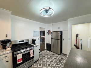 Kitchen featuring stainless steel appliances, white cabinetry, light floors, light stone counters, and ceiling fan