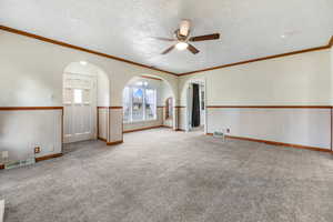 Spare room featuring a wainscoted wall, arched walkways, ceiling fan, carpet, and a textured ceiling