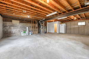 Unfinished basement featuring freestanding refrigerator, heating unit, and gas water heater