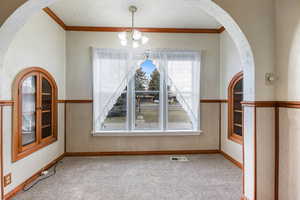 Unfurnished dining area with ornamental molding, carpet flooring, arched walkways, hanging lights, and a textured wall
