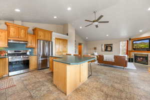 Kitchen featuring stainless steel appliances, stone finish flooring, ceiling fan, a kitchen bar, and a kitchen island