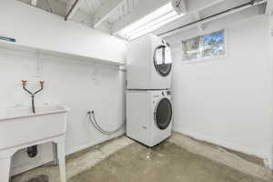 Laundry room featuring unfinished concrete floors and stacked washer / drying machine