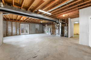 Unfinished below grade area featuring water heater, heating unit, and freestanding refrigerator