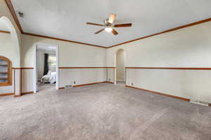 Empty room featuring arched walkways, light colored carpet, ornamental molding, ceiling fan, and a textured ceiling