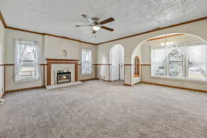 Unfurnished living room with ornamental molding, arched walkways, a tile fireplace, light carpet, and ceiling fan