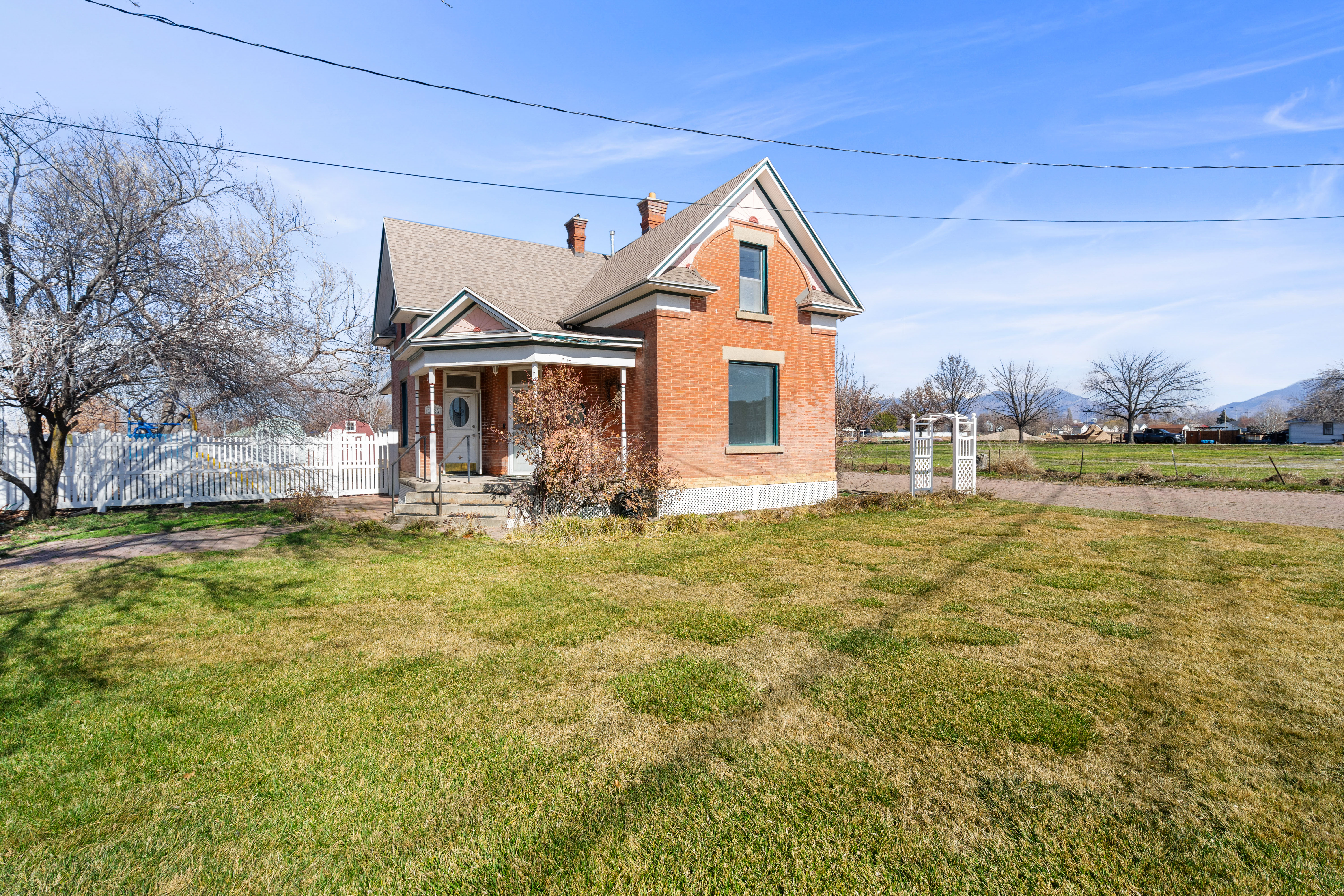 View of front facade featuring covered porch, brick siding, a chimney, and a shingled roof