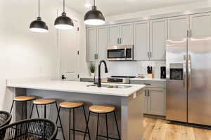 Kitchen featuring stainless steel appliances, gray cabinets, a peninsula, a breakfast bar, and hanging light fixtures