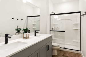 Bathroom featuring double vanity, a shower stall, and dark wood-style floors