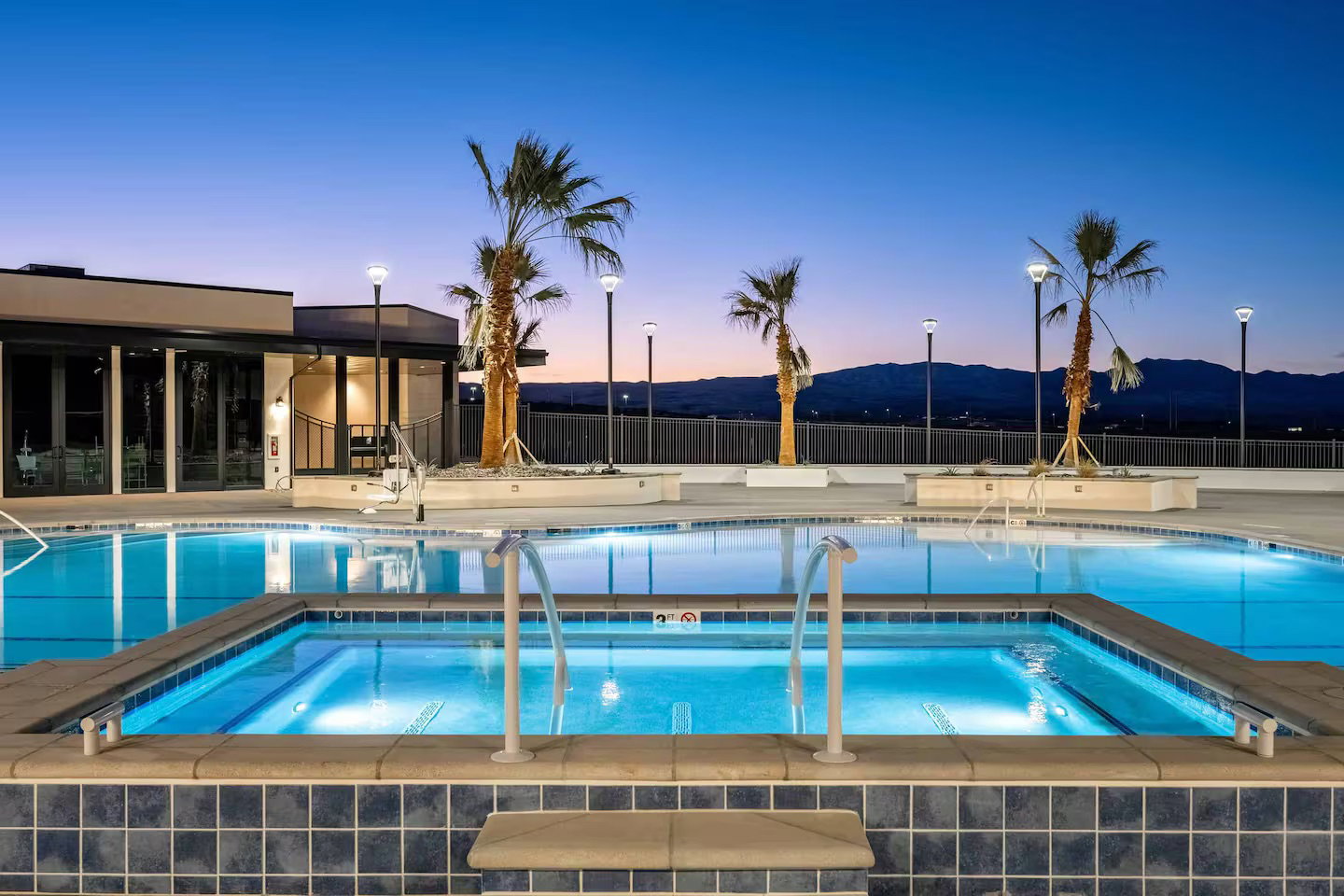 Pool at dusk with a community pool, a community hot tub, a patio, and a mountain view