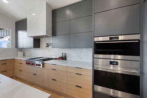 Kitchen with stainless steel appliances, modern cabinets, backsplash, and light stone counters