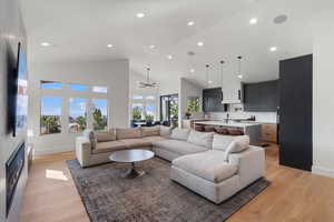 Living area featuring light wood-style flooring, recessed lighting, vaulted ceiling, and a warm lit fireplace