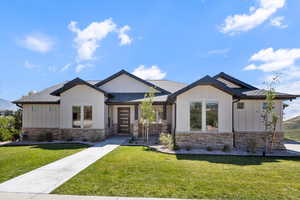 View of front of house with board and batten siding, a front yard, a shingled roof, and stone siding
