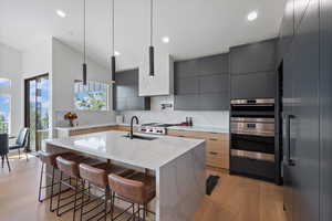 Two tone kitchen featuring modern cabinets, a kitchen island with sink, a kitchen bar, light stone counters, and pendant lighting