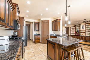 Kitchen featuring dark stone counters, hanging light fixtures, a peninsula, ceiling fan, and a kitchen bar