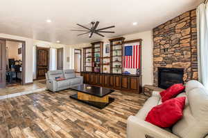 Living room with ceiling fan, a stone fireplace, and wood finished floors