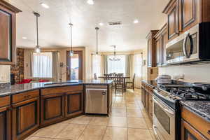 Kitchen featuring stainless steel appliances, dark stone countertops, a textured ceiling, a peninsula, and light tile patterned floors