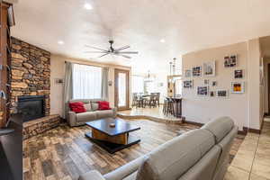 Living room featuring a ceiling fan, a textured ceiling, a fireplace, light wood finished floors, and hanging lights