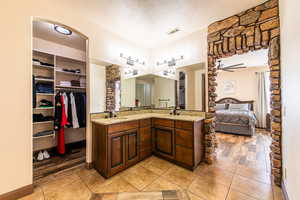 Full bath featuring a textured ceiling, double vanity, connected bathroom, a walk in closet, and light tile patterned floors