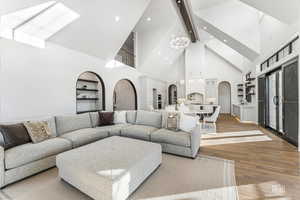 Living area with arched walkways, wood finished floors, built in shelves, a chandelier, and a skylight