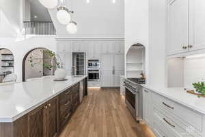 Kitchen featuring light stone counters, light wood finished floors, a high ceiling, stainless steel appliances, and two tone cabinets