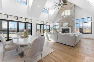 Dining space with light wood finished floors, a fireplace, french doors, ceiling fan, and vaulted ceiling