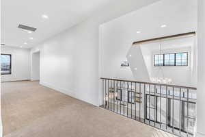 Hallway with light colored carpet, healthy amount of natural light, and suspended lighting